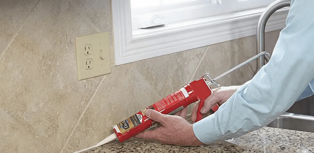 Handyman applying caulk along a kitchen backsplash and countertop seam in Columbia, MO