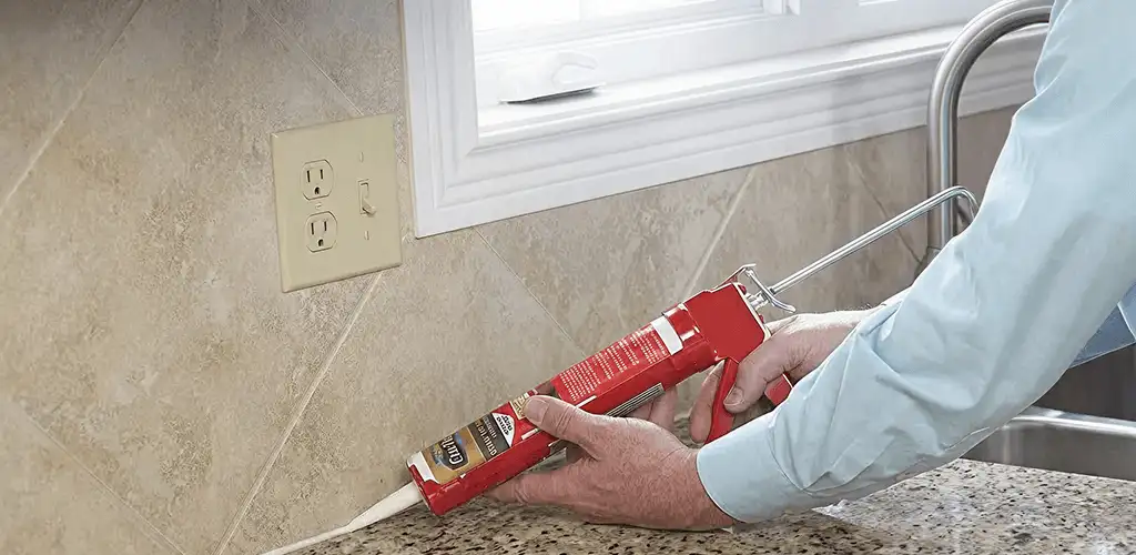 Handyman applying caulk along a kitchen backsplash and countertop seam in Columbia, MO